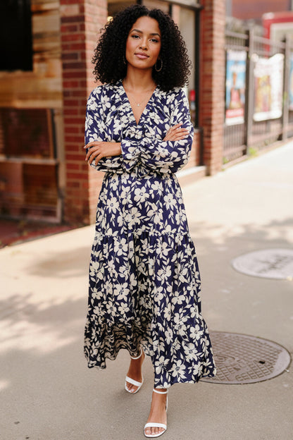 Woman wearing a blue floral dress standing on a sidewalk.