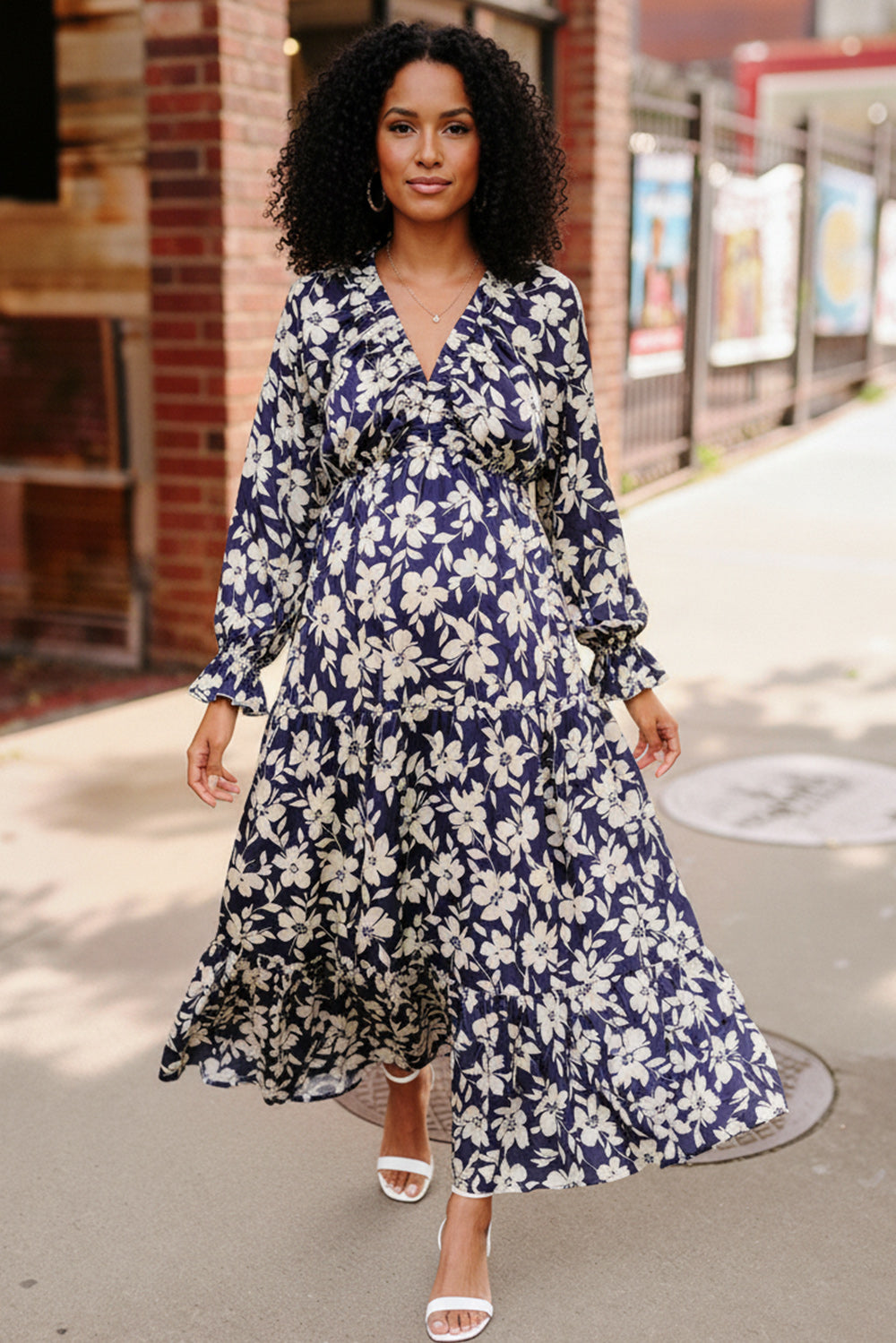 Woman wearing a blue floral dress standing on a sidewalk.