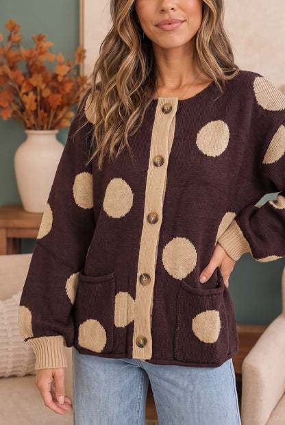A woman wearing a dark brown knit cardigan with large beige polka dots and a beige button placket, paired with light blue jeans in a cozy indoor setting.