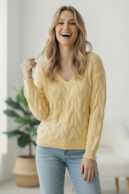 Woman wearing a yellow cable knit sweater and light blue jeans indoors.