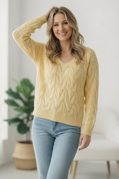Woman wearing a yellow cable knit sweater and light blue jeans indoors.