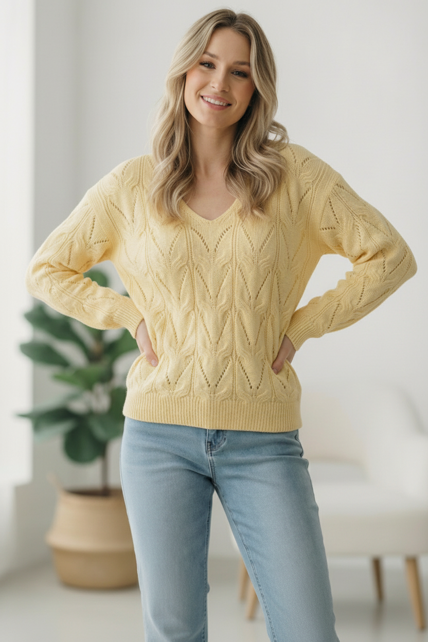 Woman wearing a yellow cable knit sweater and light blue jeans indoors.