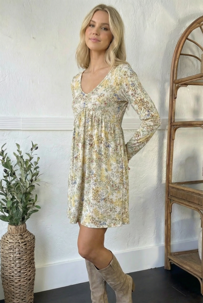 Woman wearing a floral dress standing in a room with a plant and wooden shelf.