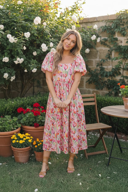 Woman in a floral dress standing in a garden with flowers and a table in the background