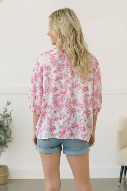 Woman wearing a pink floral blouse and denim shorts in a minimal indoor setting.