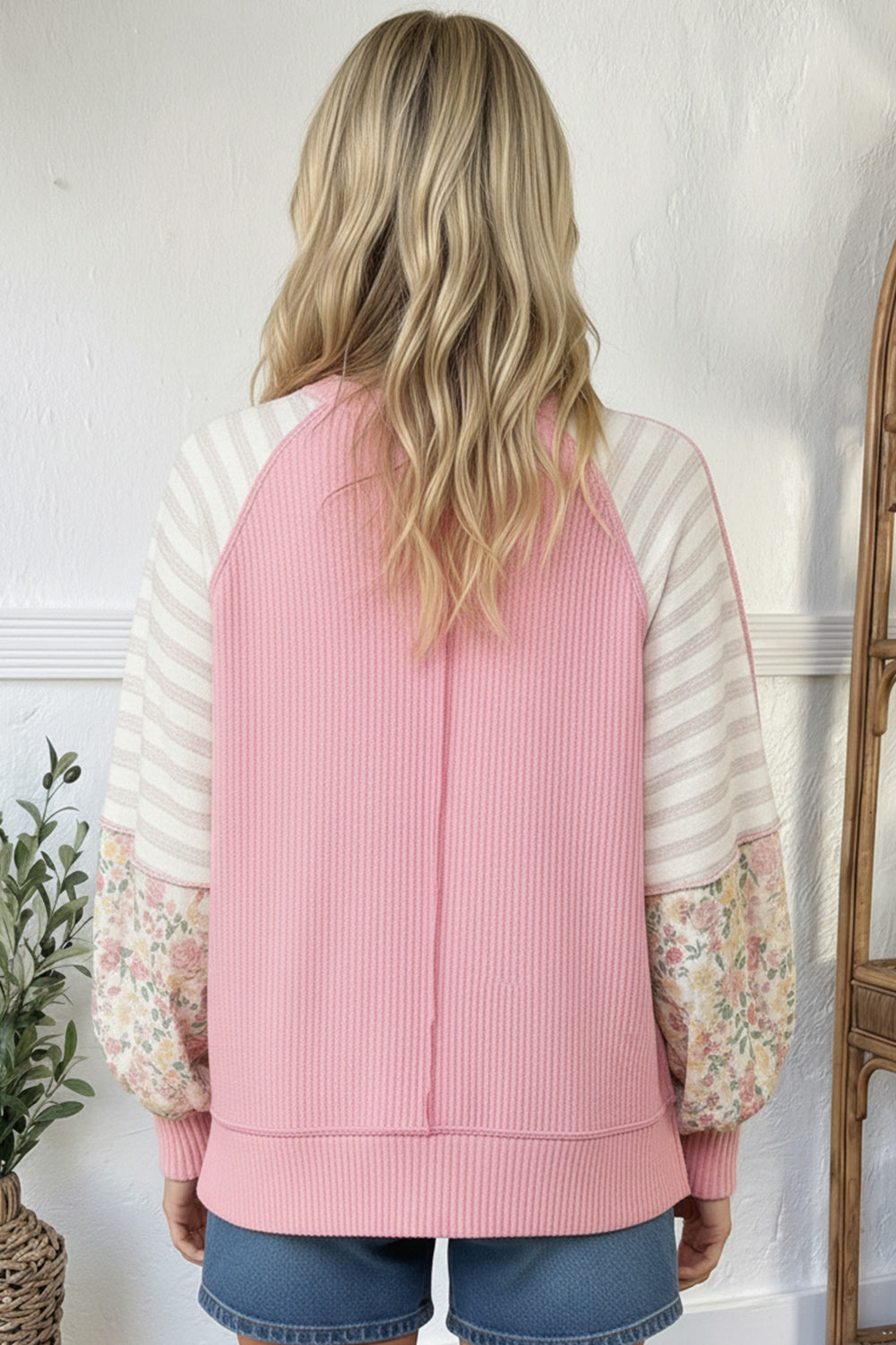 Person wearing a pink and white striped sweater with floral sleeves against a white wall.