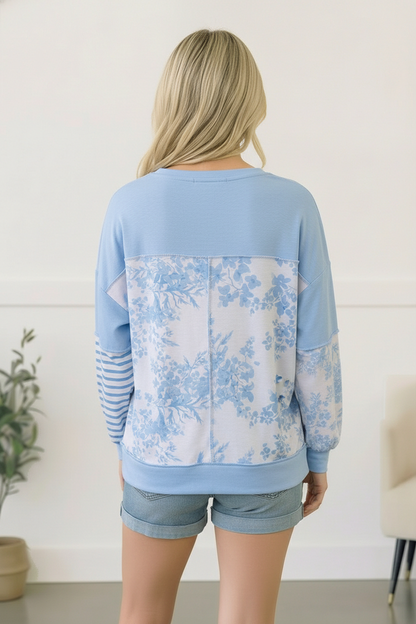 Woman wearing a light blue floral-patterned sweatshirt with a white background