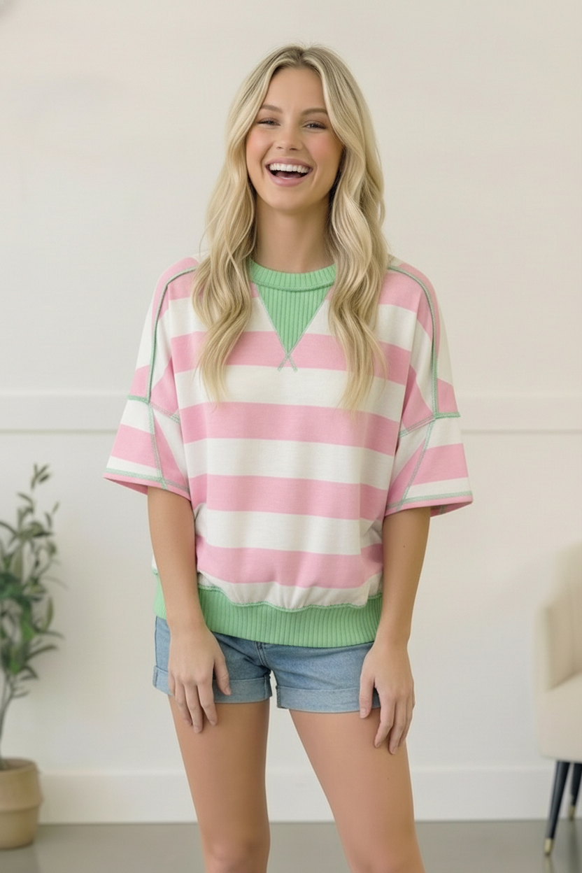 Woman wearing a pink and white striped sweater with green accents indoors.