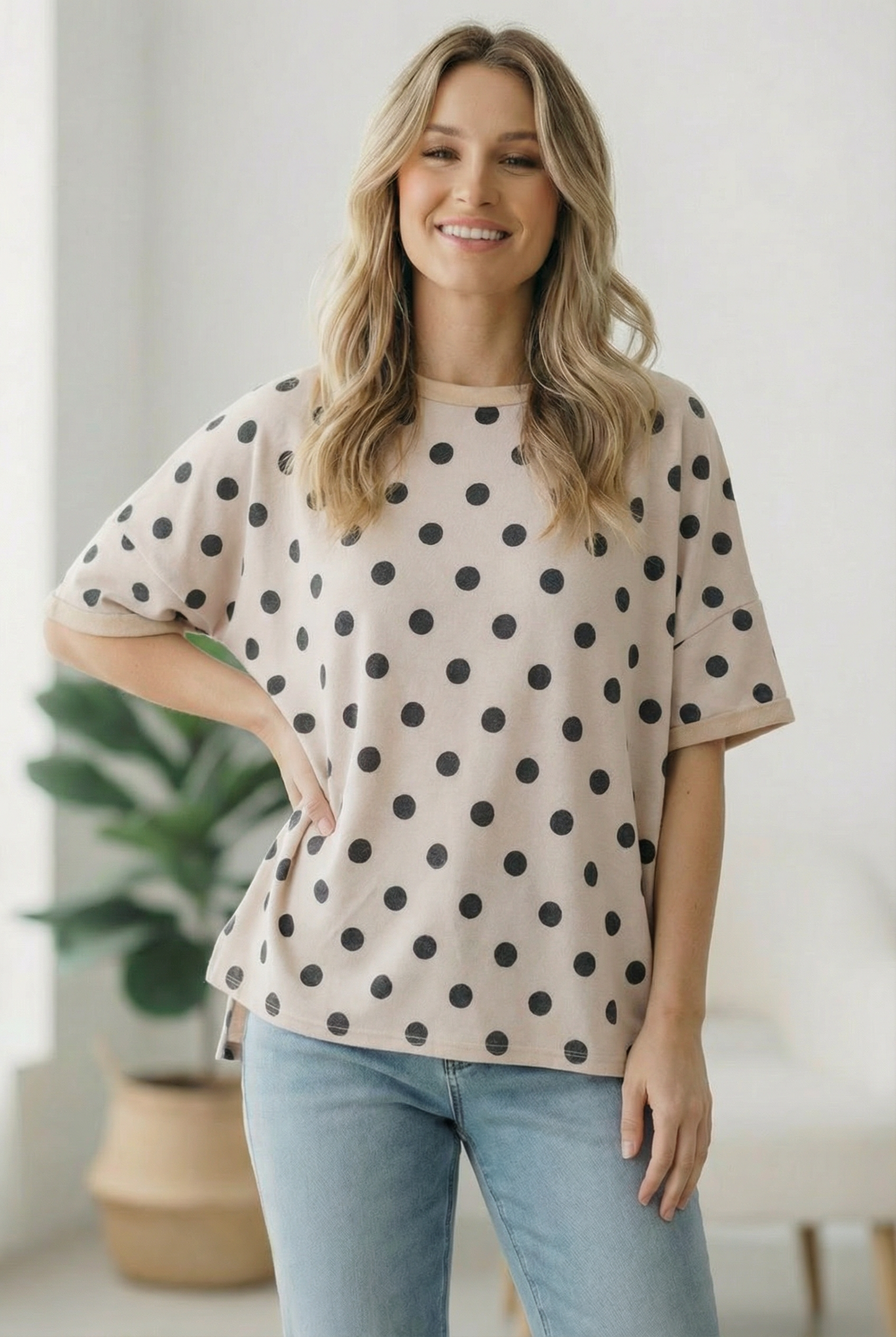 Woman wearing a beige t-shirt with black polka dots and light blue jeans indoors.