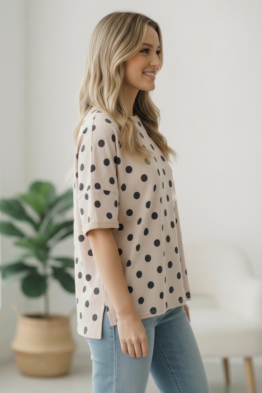 Woman wearing a beige blouse with black polka dots and light blue jeans indoors.