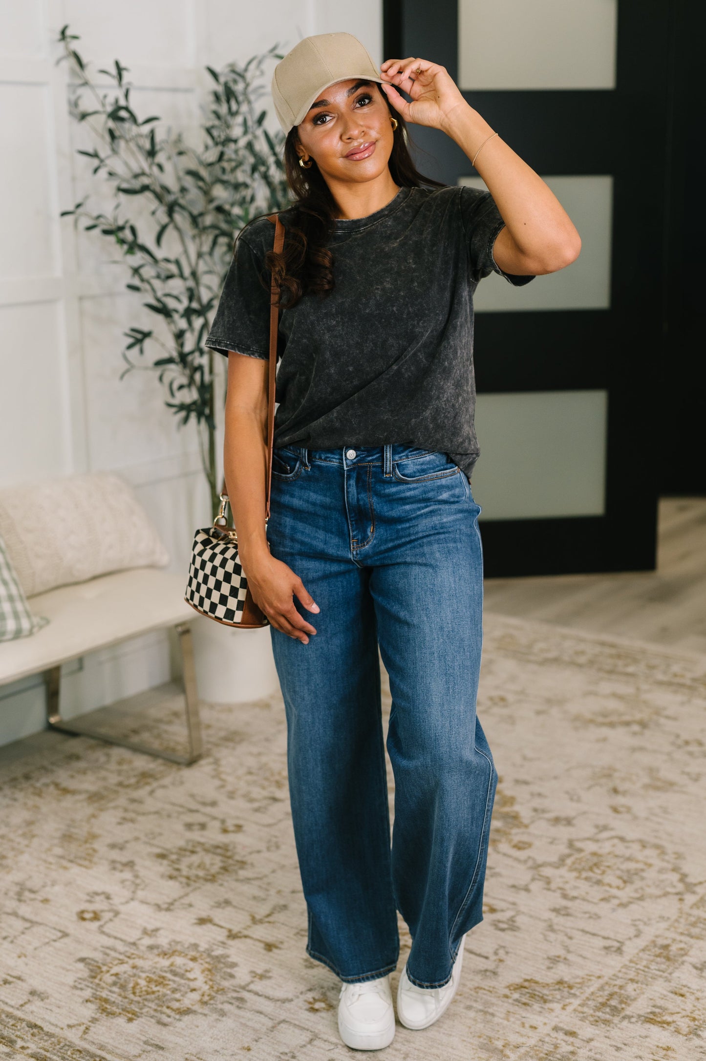 Woman wearing a black t-shirt, blue jeans, and a beige cap indoors.