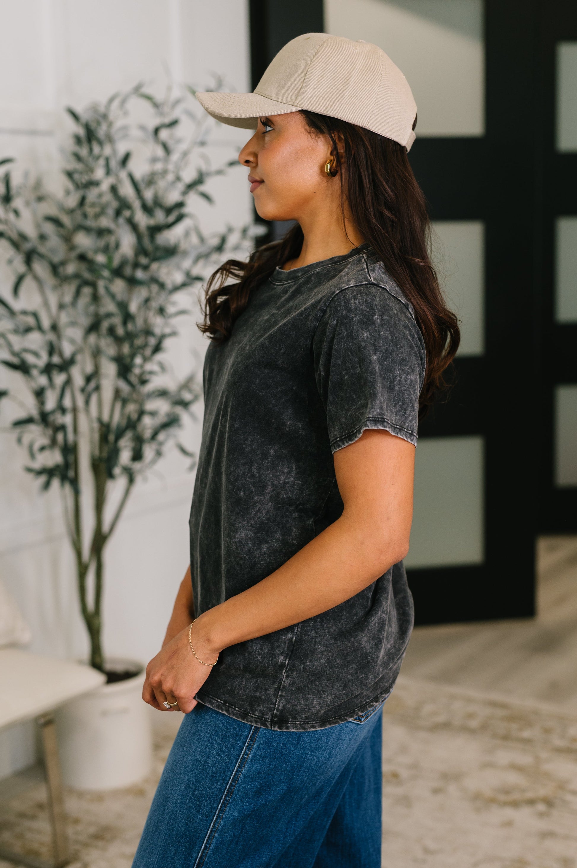 Woman wearing a beige cap and black acid-wash shirt in an indoor setting