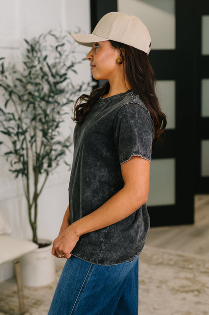 Woman wearing a beige cap and black acid-wash shirt in an indoor setting