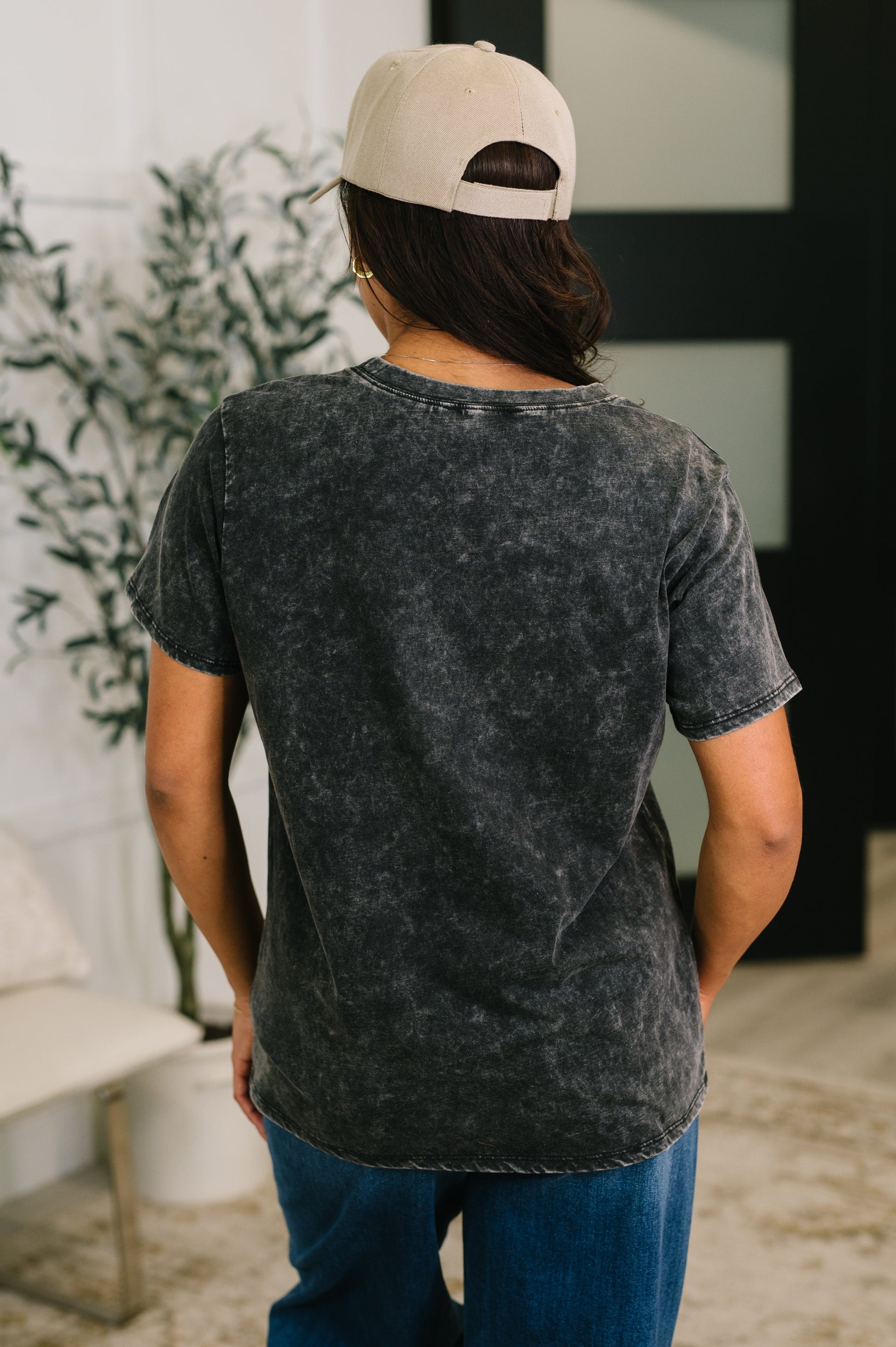 Person wearing a black acid-wash t-shirt and beige cap indoors