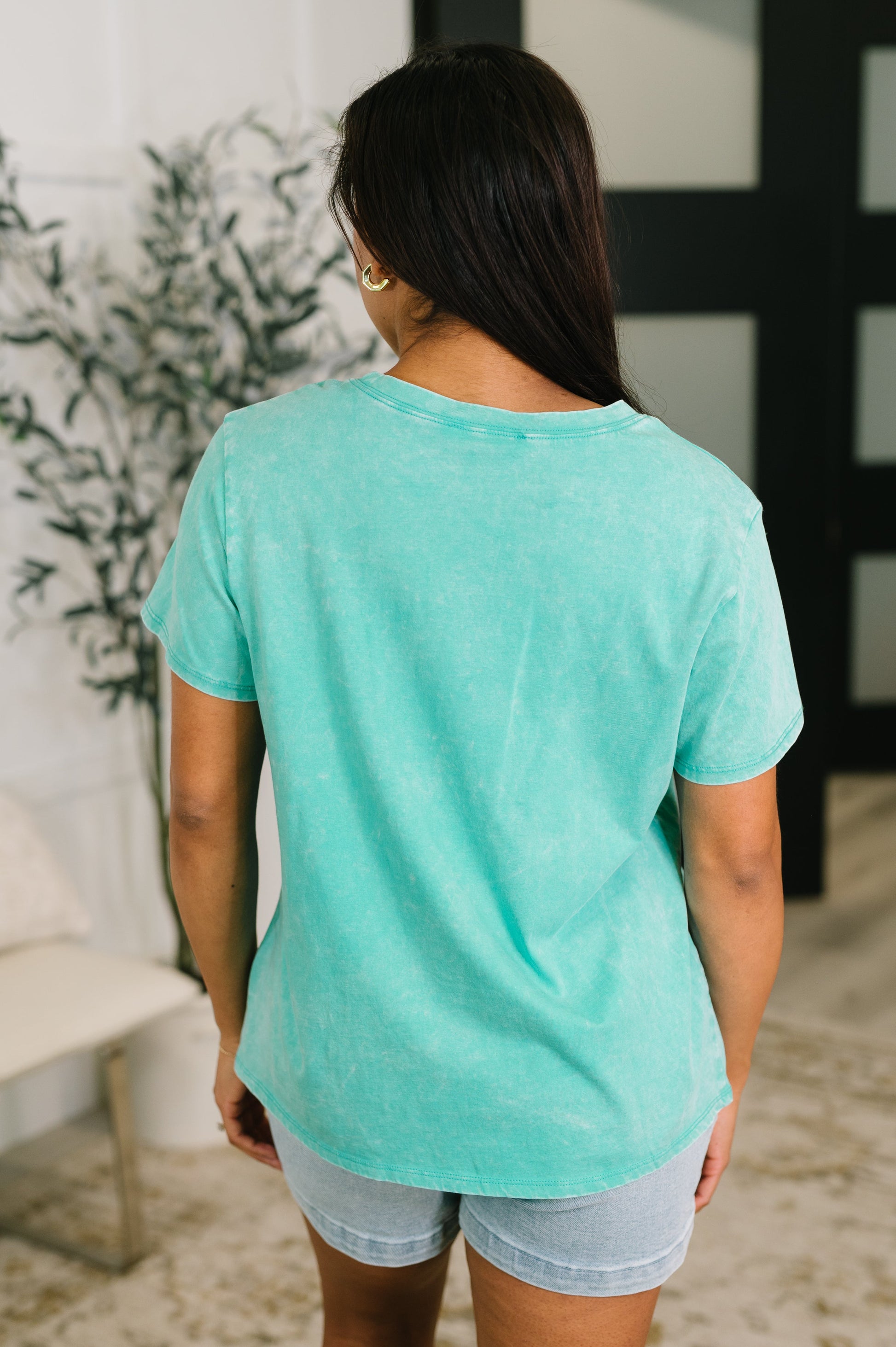 Person wearing a teal t-shirt and light blue shorts in an indoor setting.
