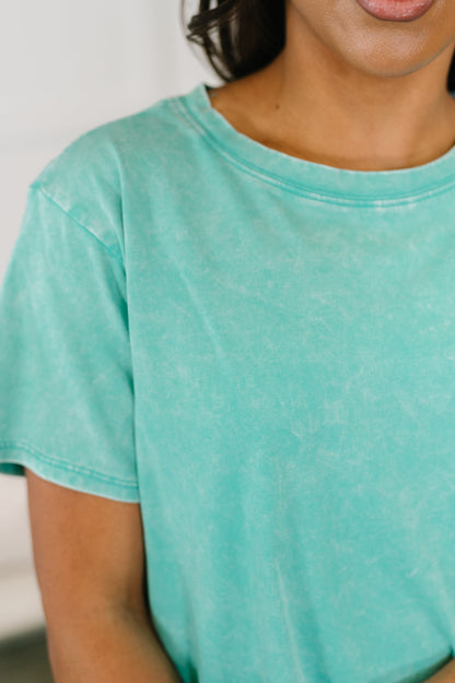 Person wearing a teal t-shirt with a blurred background
