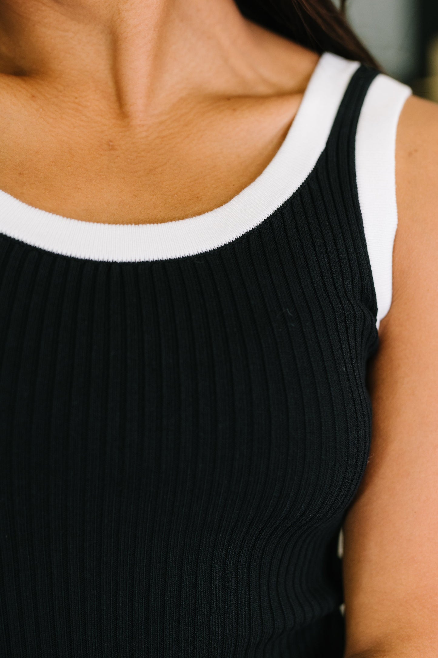 Black ribbed tank top with white trim worn by a person.