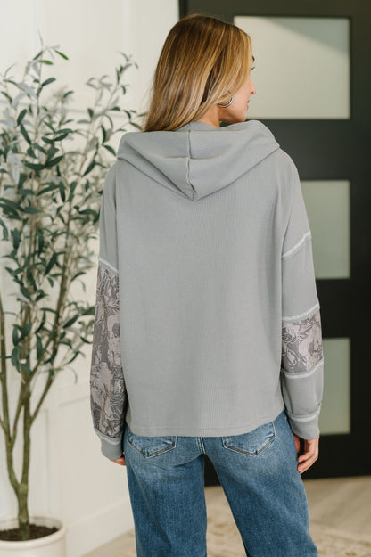 Person wearing a gray hoodie with lace sleeves in a room with a plant and framed picture.