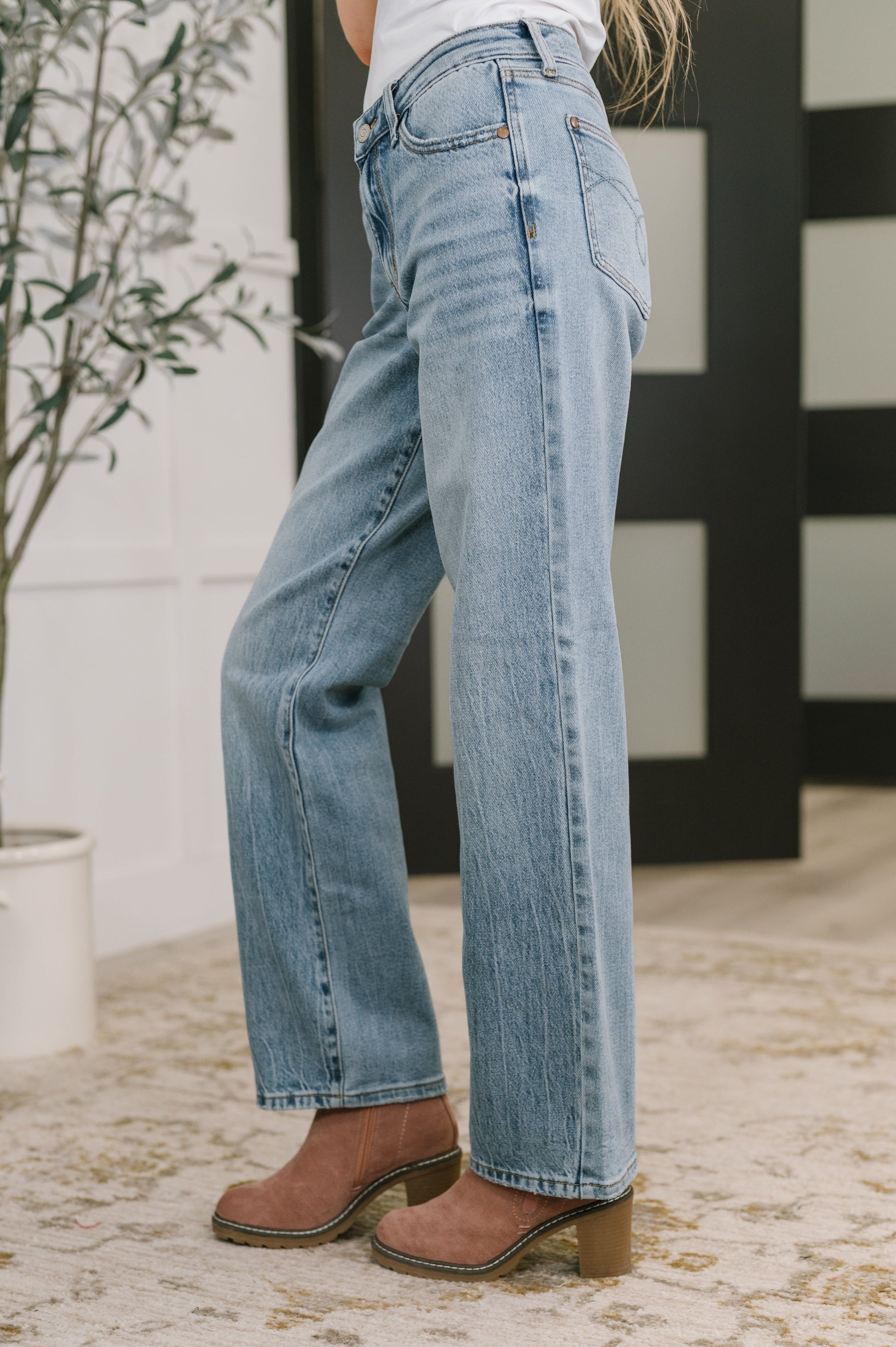 Person wearing light blue jeans and brown shoes indoors with a plant in the background
