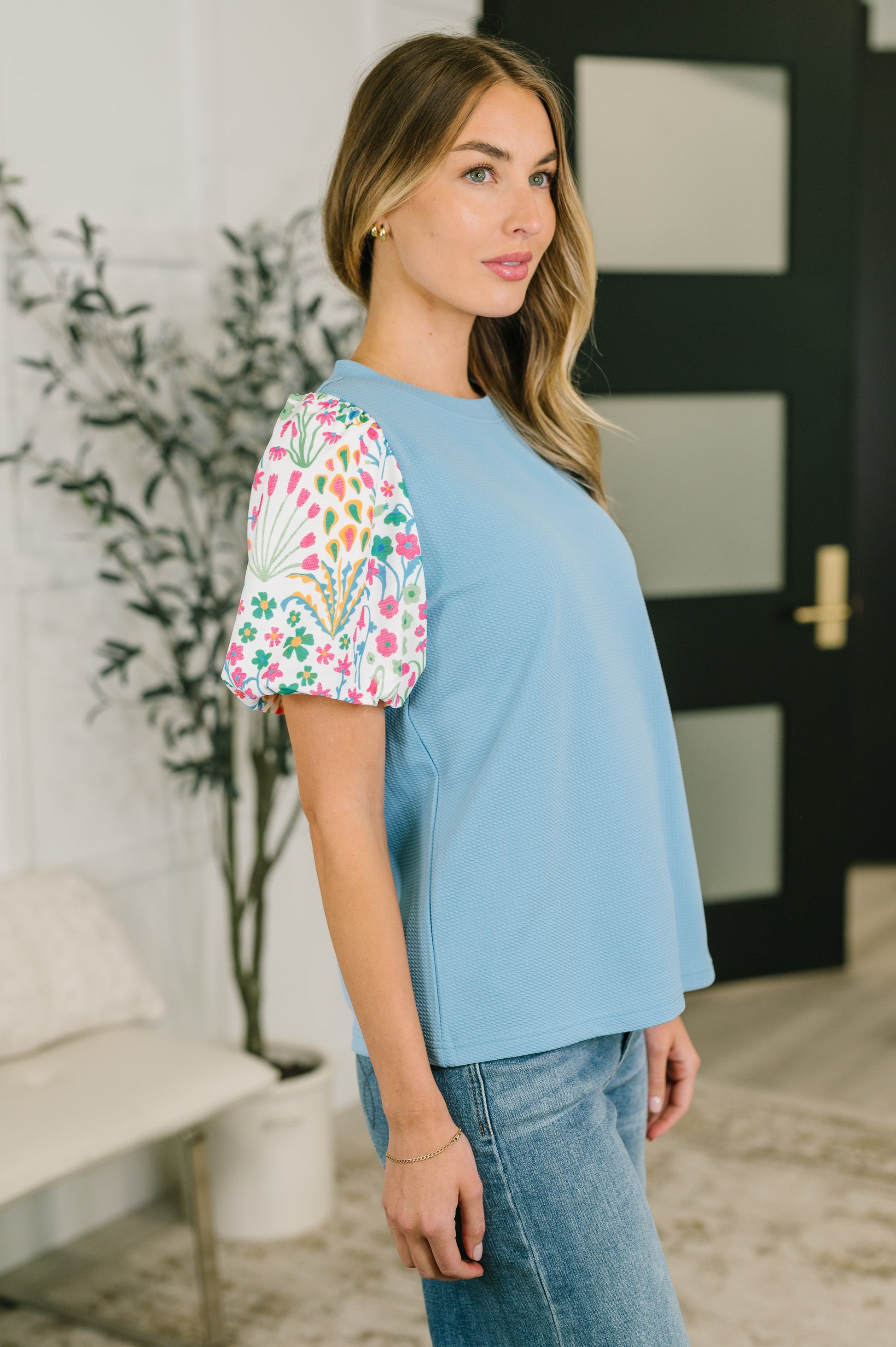 Woman wearing a light blue top with floral sleeves in an indoor setting.