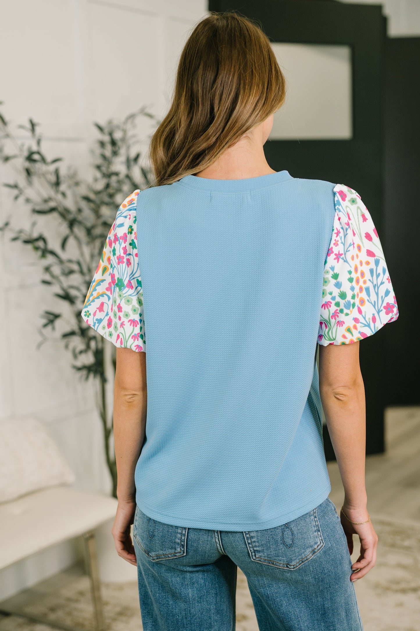 Person wearing a light blue top with colorful sleeves in an indoor setting