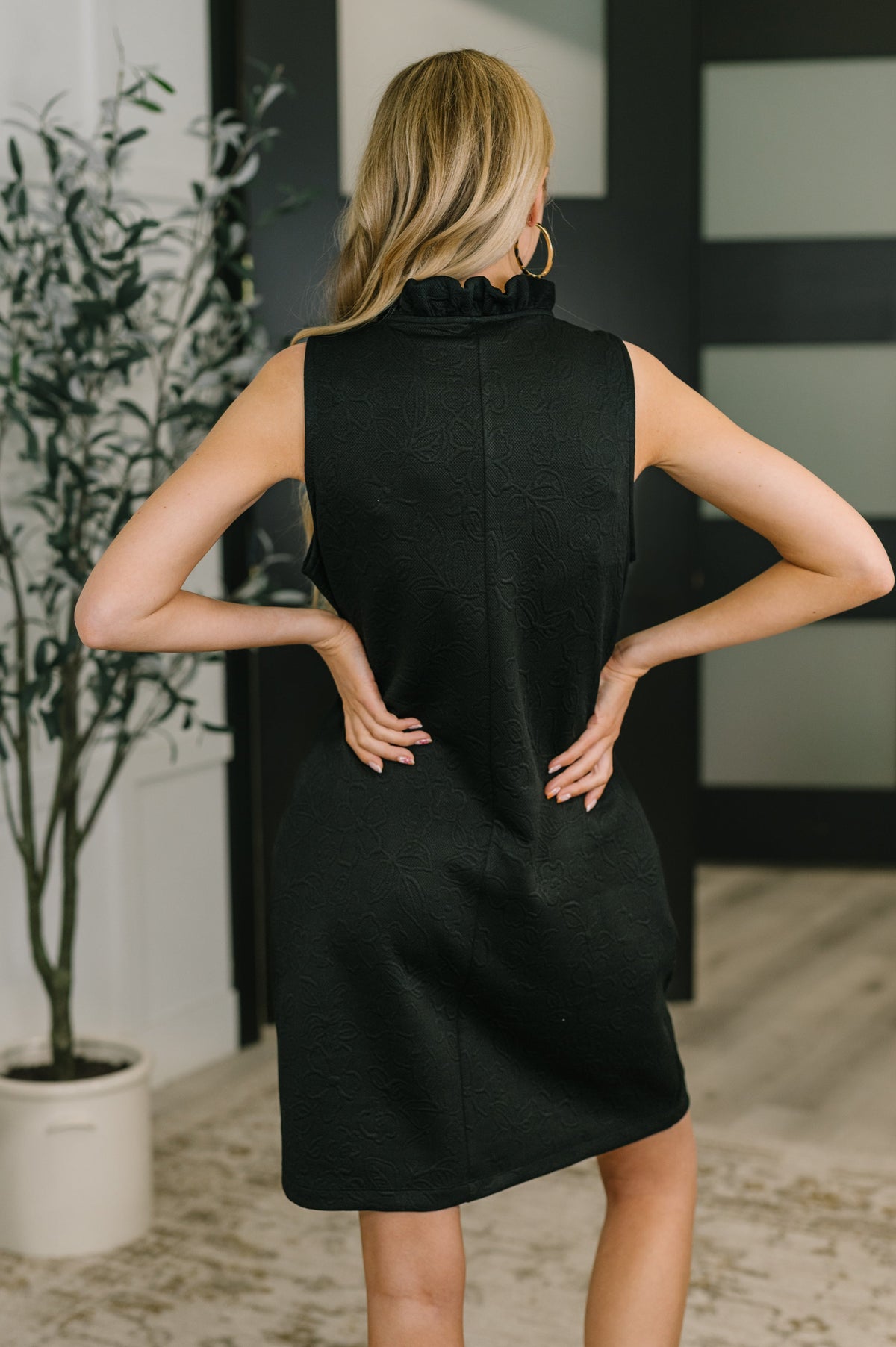 Woman wearing a black sleeveless dress in an indoor setting.