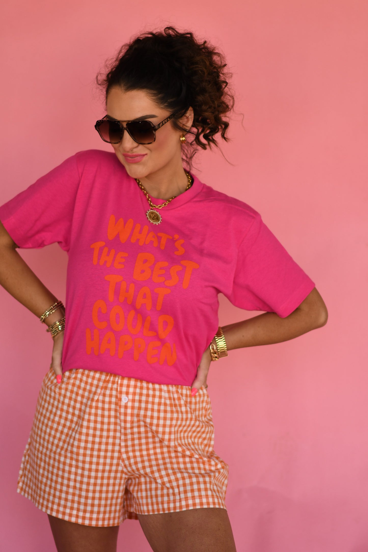 Woman wearing a pink t-shirt with text and orange checkered shorts against a pink background