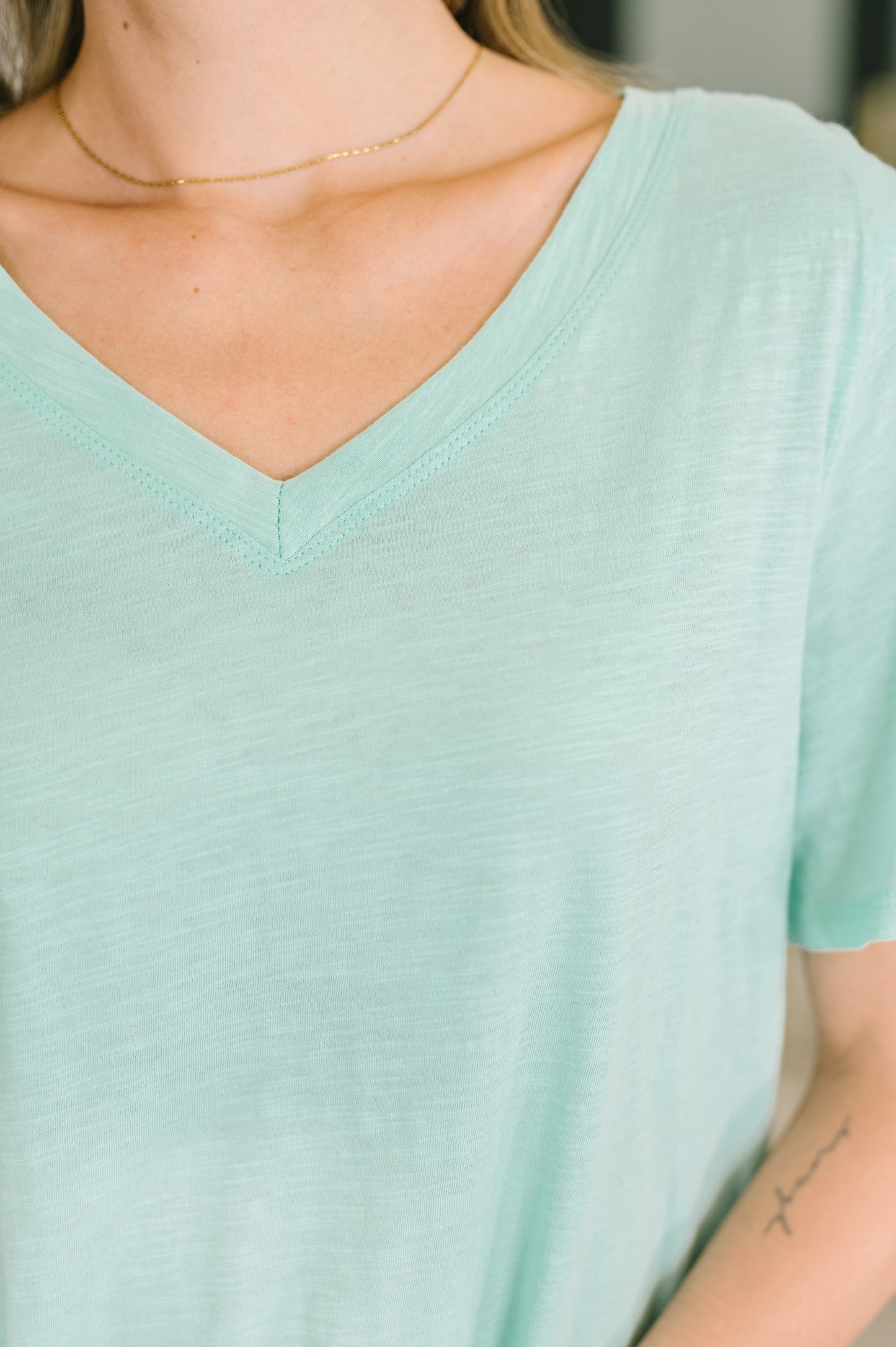 Person wearing a light green t-shirt with a blurred background