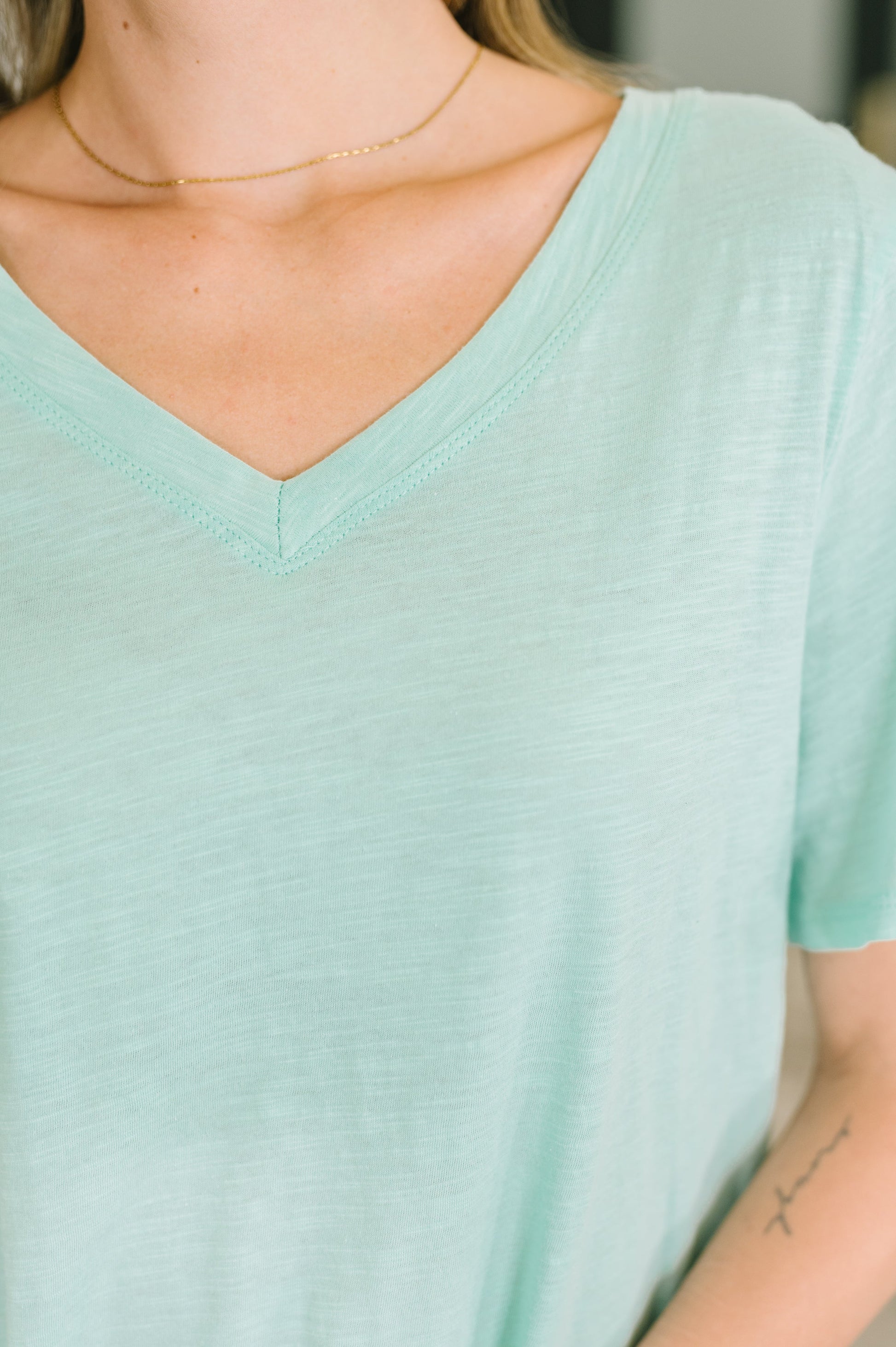 Person wearing a light green t-shirt with a blurred background