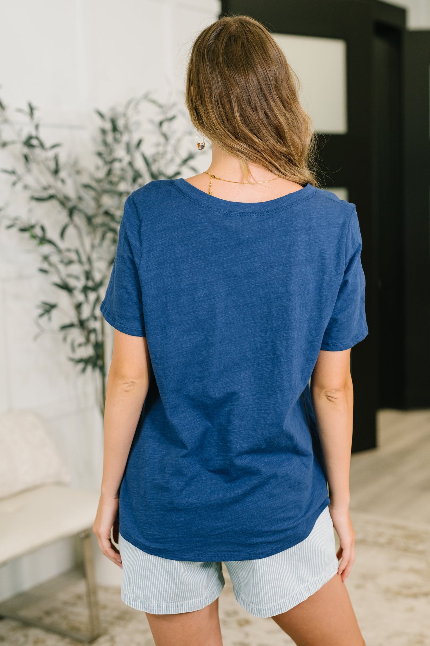 Woman wearing a blue t-shirt and light shorts indoors with a plant in the background