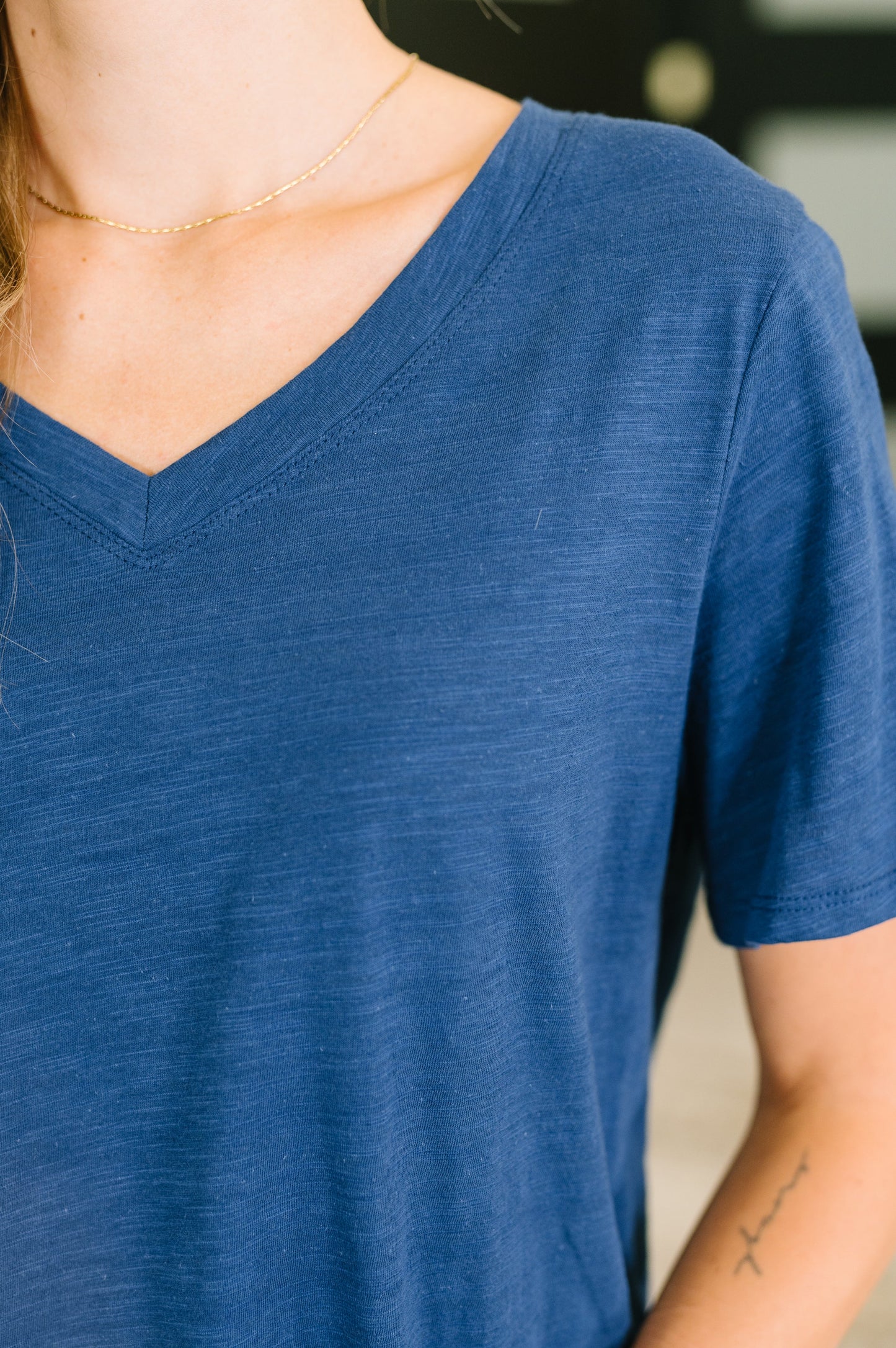 Close-up of a person wearing a blue V-neck shirt with a blurred background
