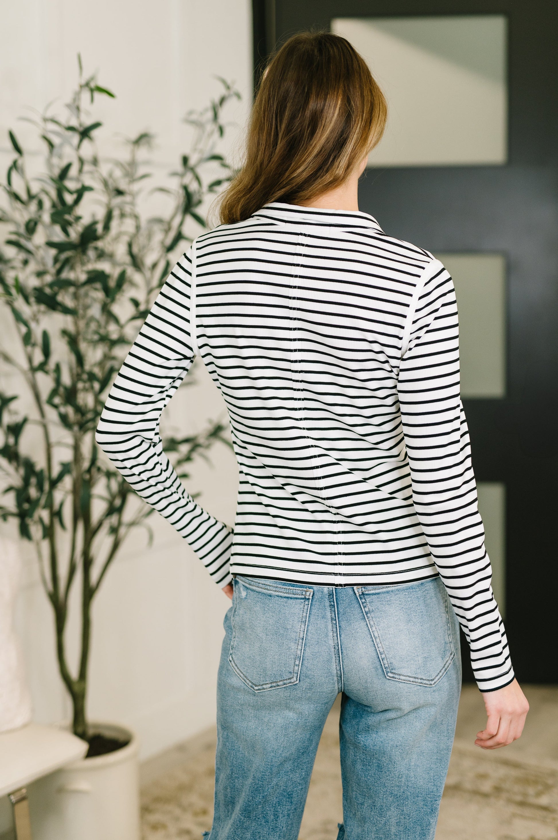 Person wearing a black and white striped long-sleeve top and blue jeans, standing indoors.