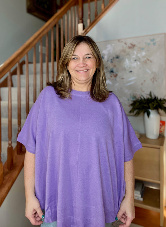 Woman wearing a purple shirt standing in a home setting with a staircase and decor.