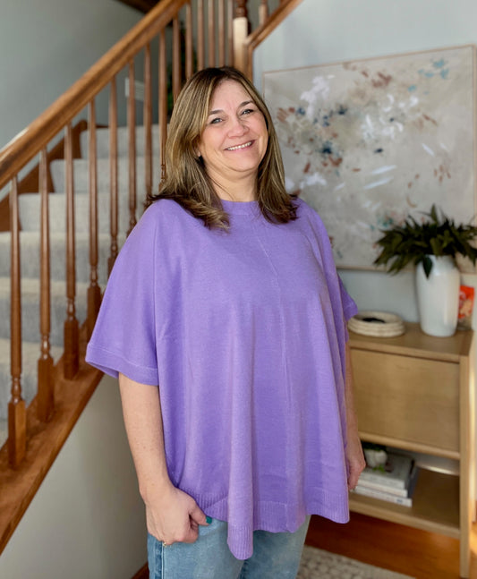 Woman wearing a purple shirt standing in a home interior with a staircase and decor.