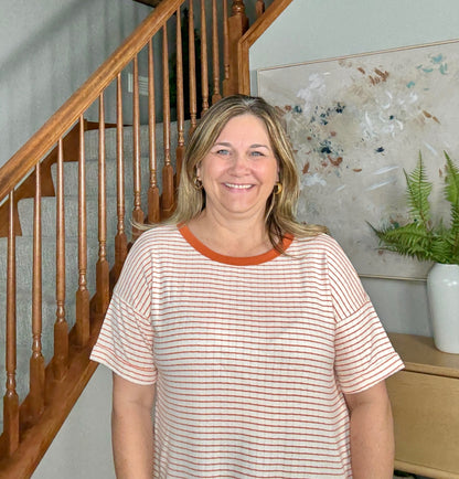Woman standing in a home setting with wooden staircase and decorative elements.