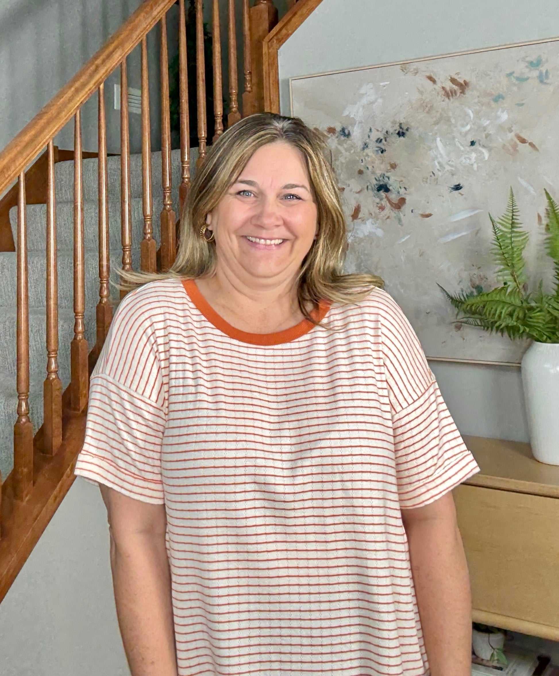 Woman standing in a home setting with a staircase and decorative items in the background