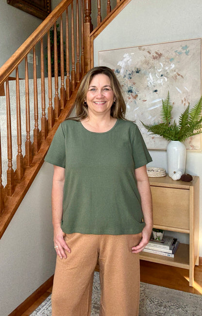 Woman wearing a green top and brown pants standing in a home interior.
