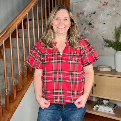 Woman wearing a red plaid shirt standing in a home interior with a staircase and decor.