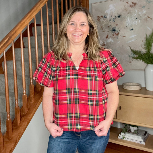 Woman wearing a red plaid shirt standing in a home interior with a staircase and decor.