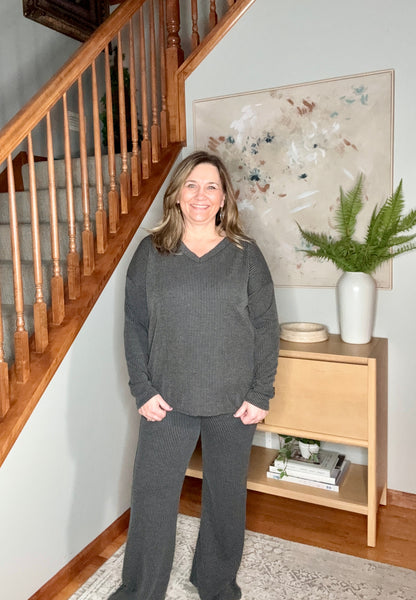 Woman in a gray outfit standing in a home interior with a staircase and decor.