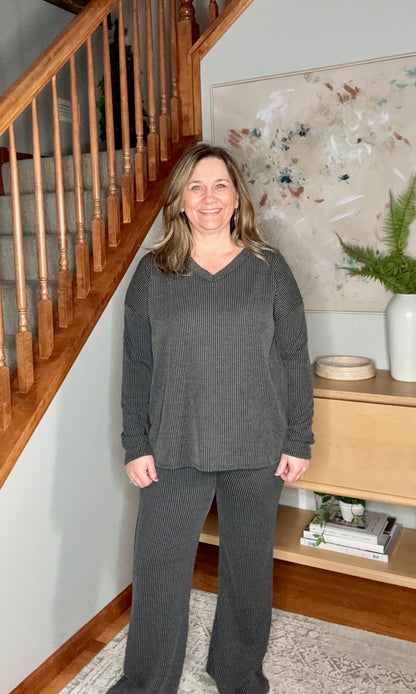 Woman in gray outfit standing in a home interior with wooden staircase and decor.