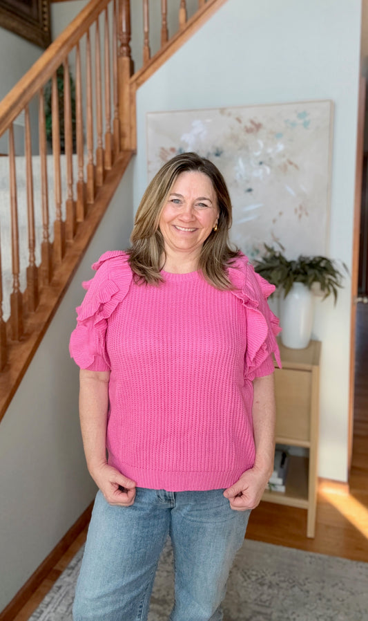 Woman wearing a pink top with ruffled sleeves in a home setting.