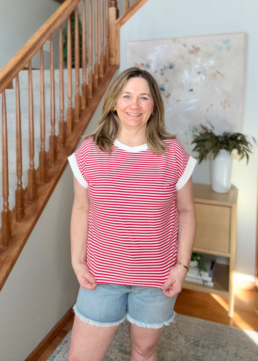Woman wearing a red and white striped shirt and denim shorts standing in a home setting.