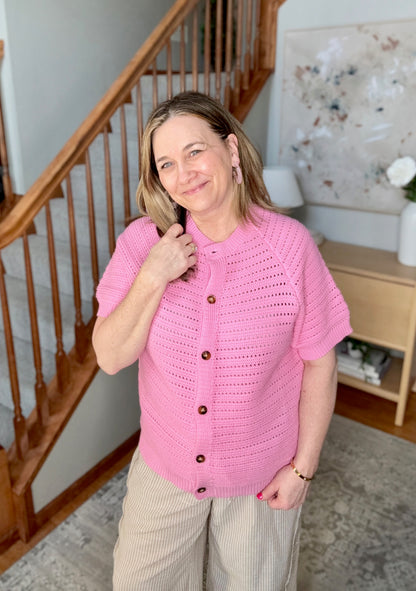 Woman wearing a pink knitted cardigan with buttons indoors, near a staircase.