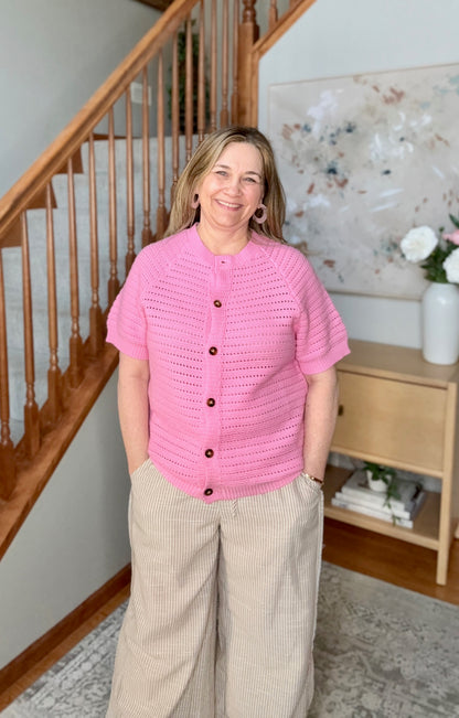 Woman wearing a pink crochet cardigan standing in a home interior.