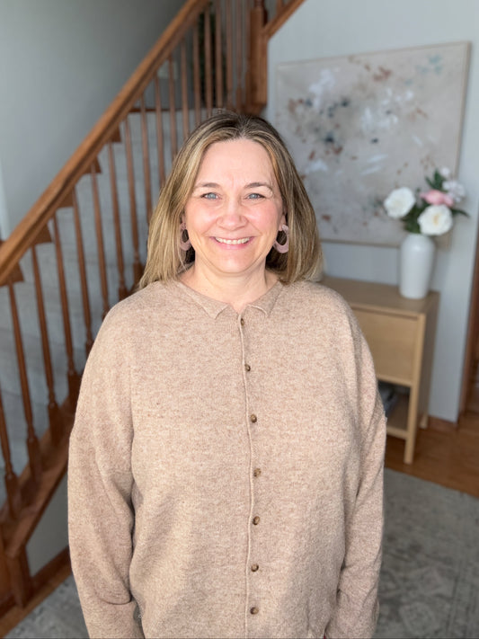 Woman standing in a home interior with a staircase and floral arrangement in the background