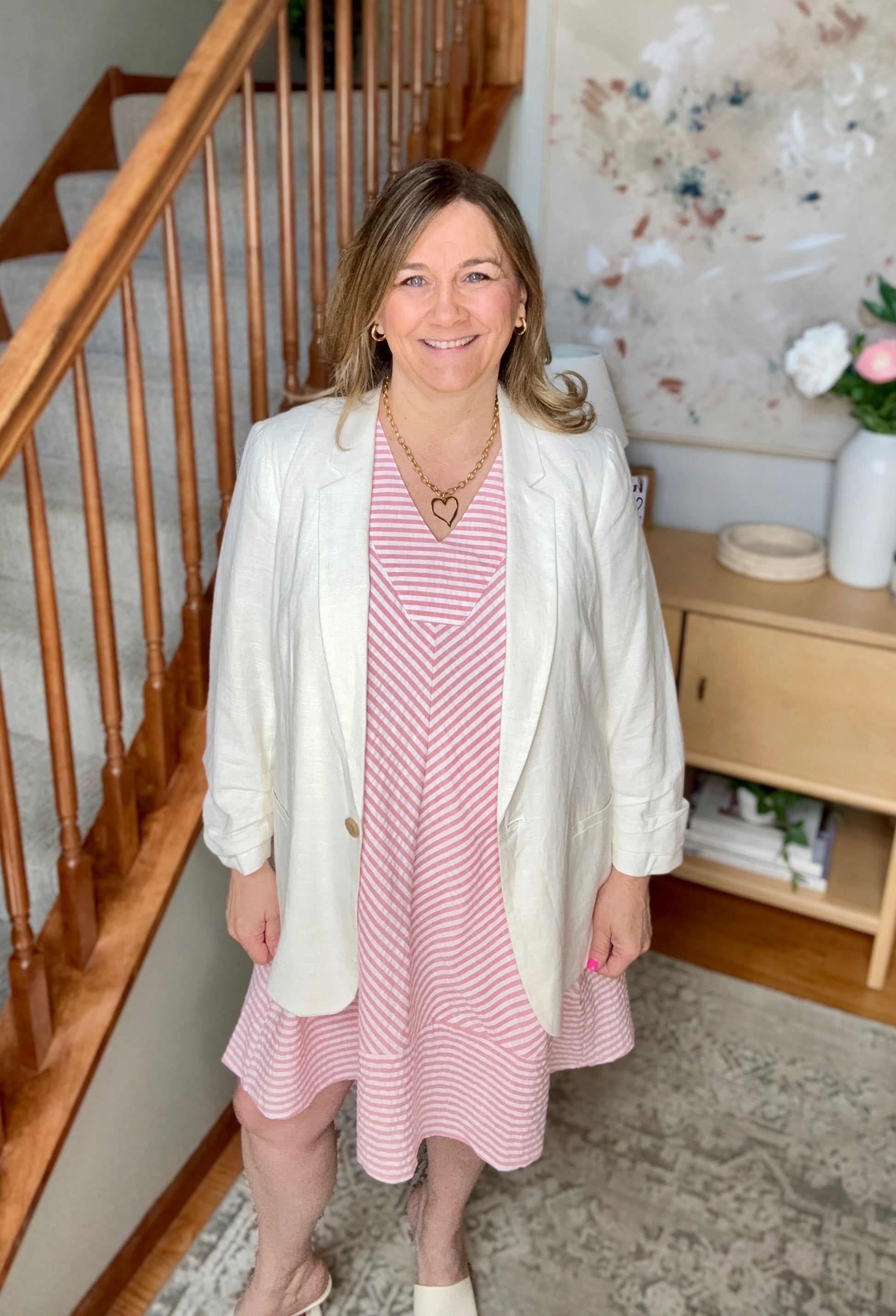 Woman in a pink dress with a white cardigan standing in a home setting.