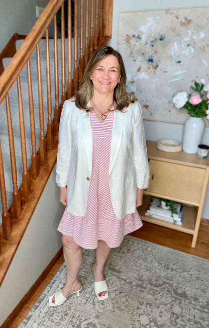 Woman in a pink dress with a white cardigan standing in a home setting.