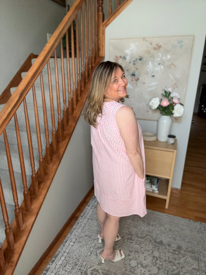 Woman in a pink striped dress standing in a home interior with wooden staircase and floral decorations.