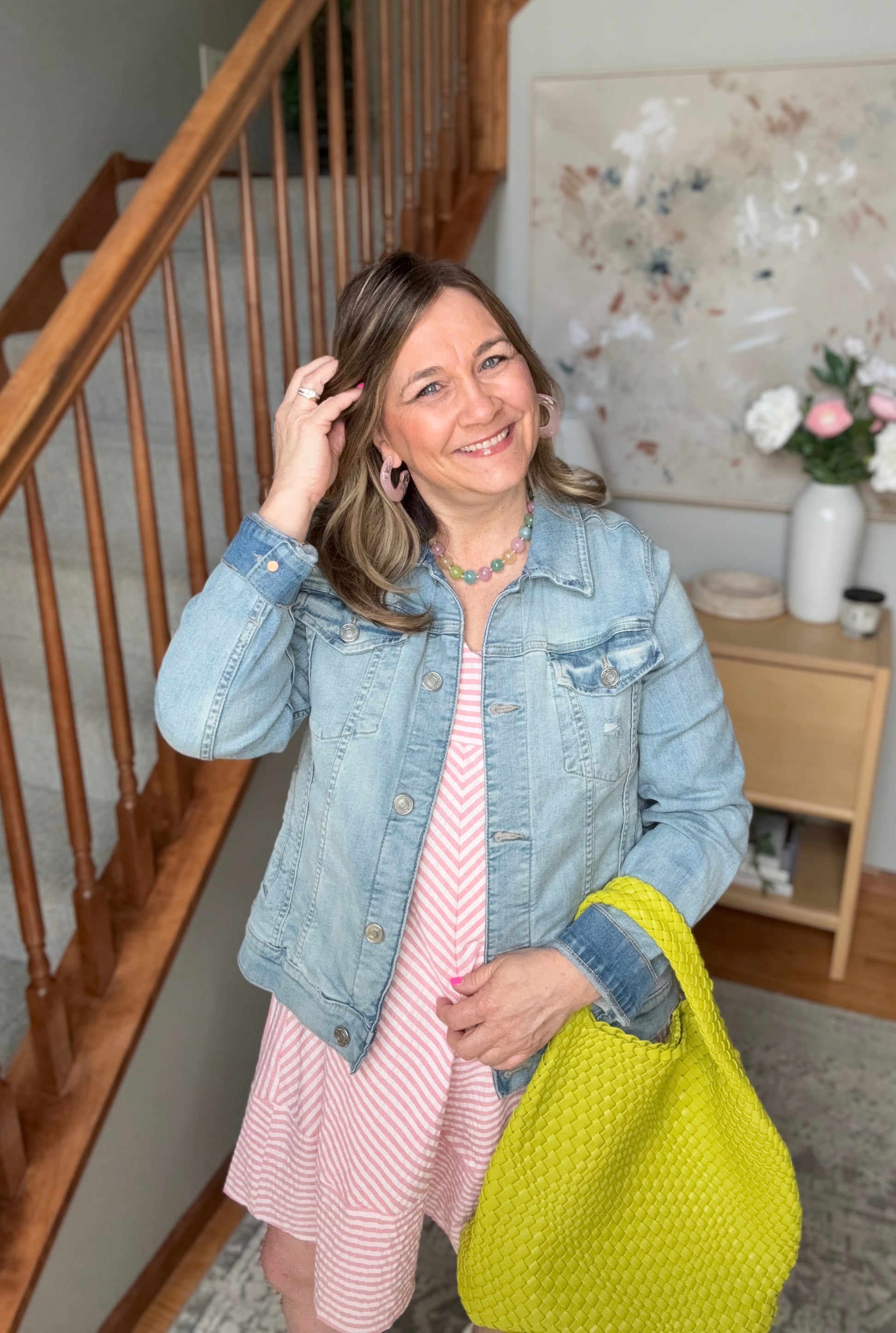Woman holding a bright yellow bag indoors, with a staircase and decorative items in the background.